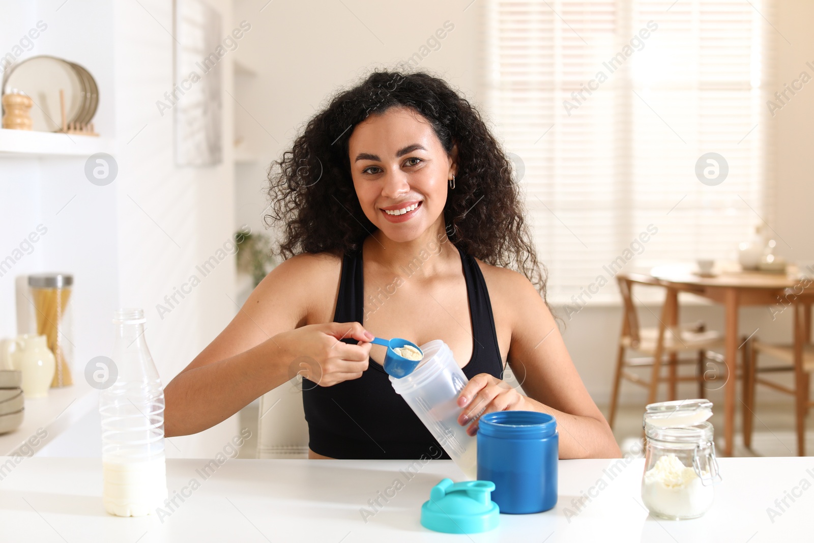 Photo of Beautiful woman making protein shake at white table indoors