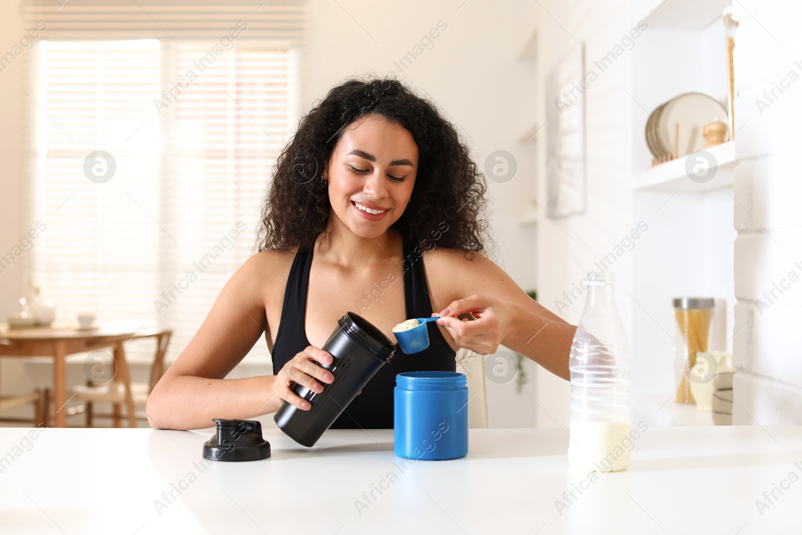 Photo of Beautiful woman making protein shake at white table indoors