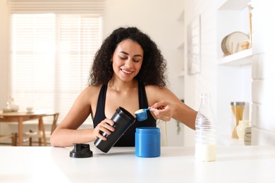 Photo of Beautiful woman making protein shake at white table indoors