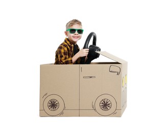 Little boy in sunglasses driving car made of cardboard on white background