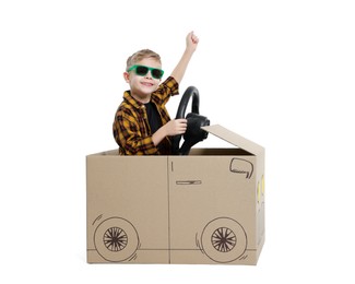 Photo of Little boy in sunglasses driving car made of cardboard on white background