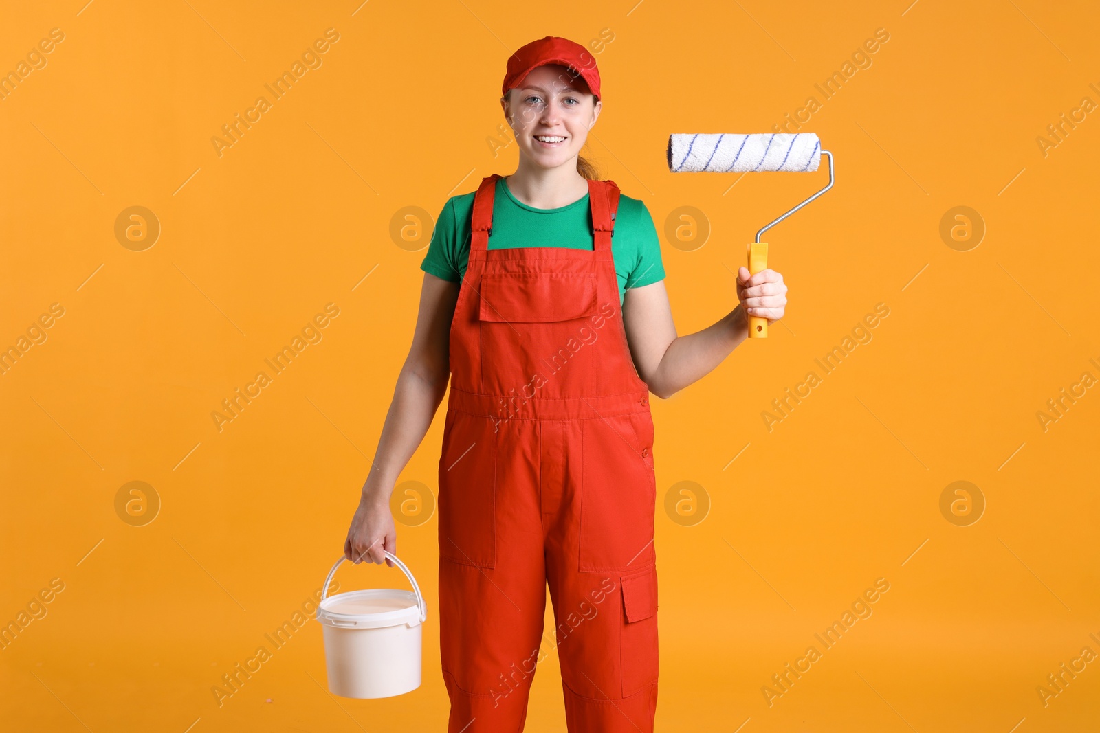 Photo of Professional painter with roller and bucket of paint on orange background