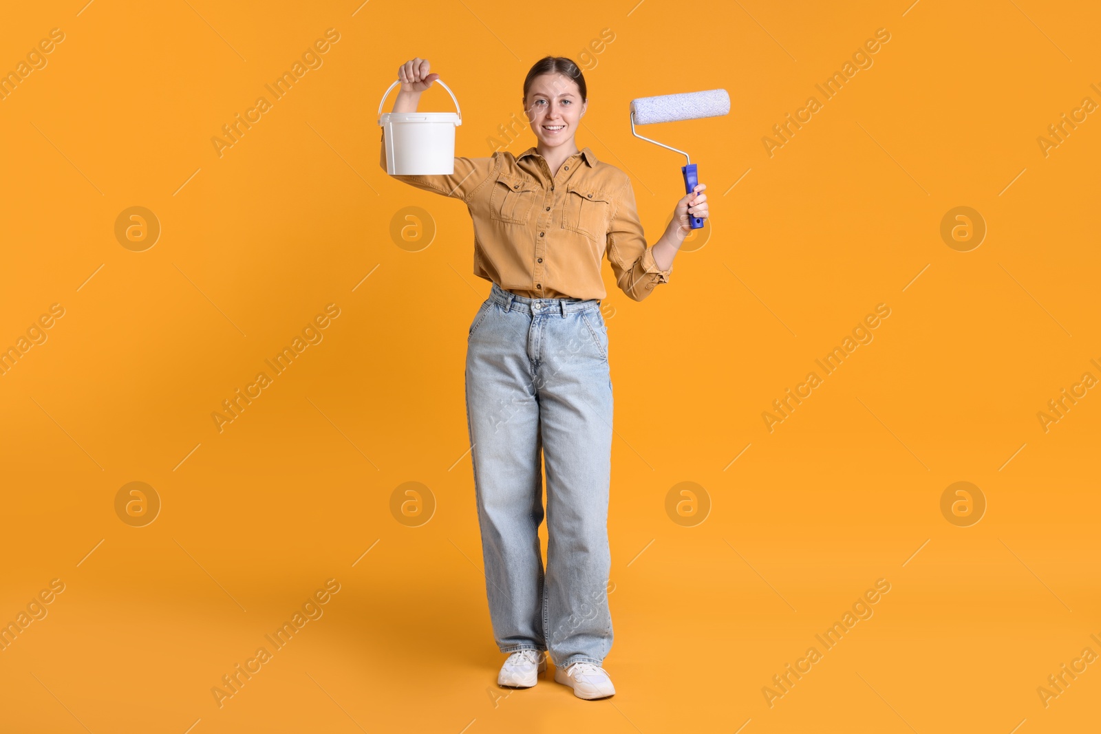 Photo of Woman with roller and bucket of paint on orange background