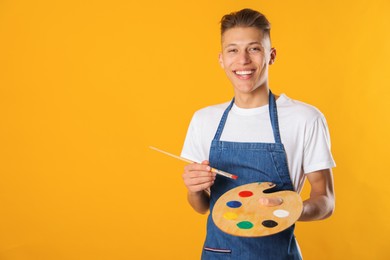 Photo of Happy man with wooden palette and paintbrush on orange background. Space for text