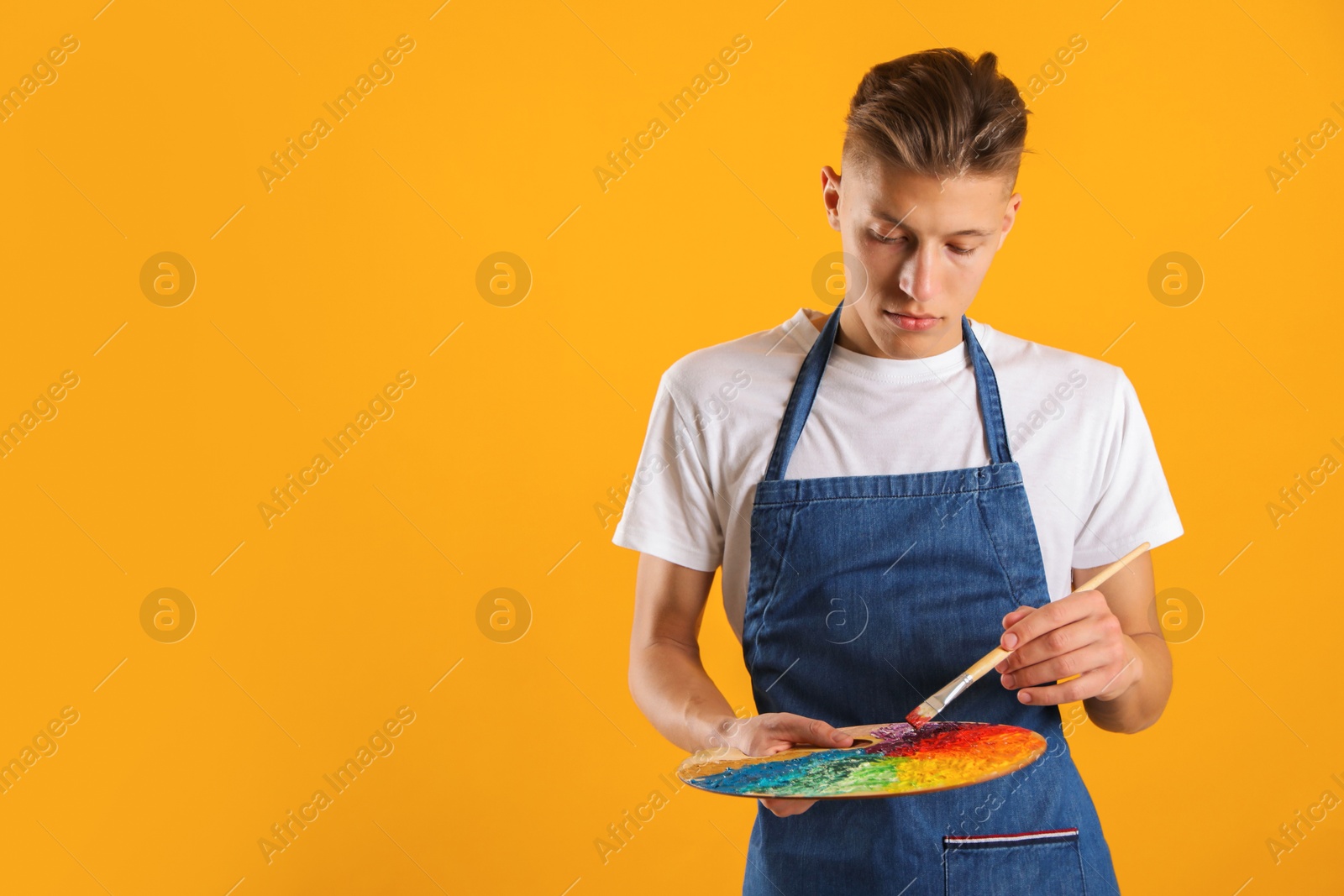 Photo of Man with palette and paintbrush on orange background. Space for text