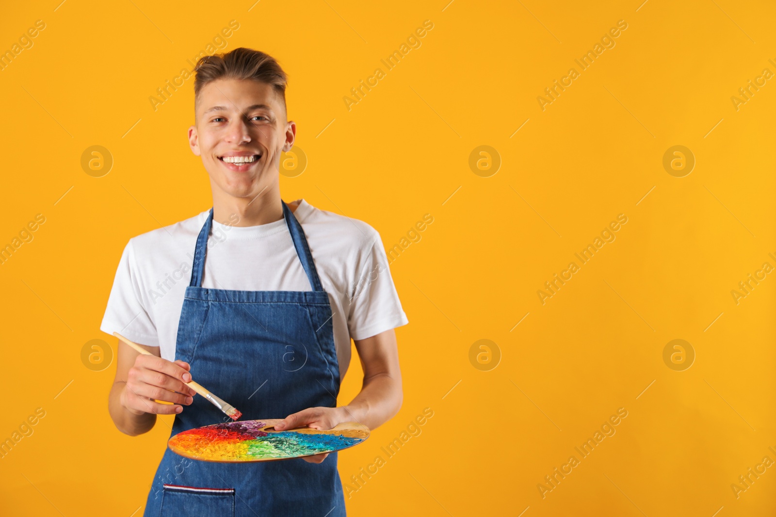 Photo of Happy man with palette and paintbrush on orange background. Space for text