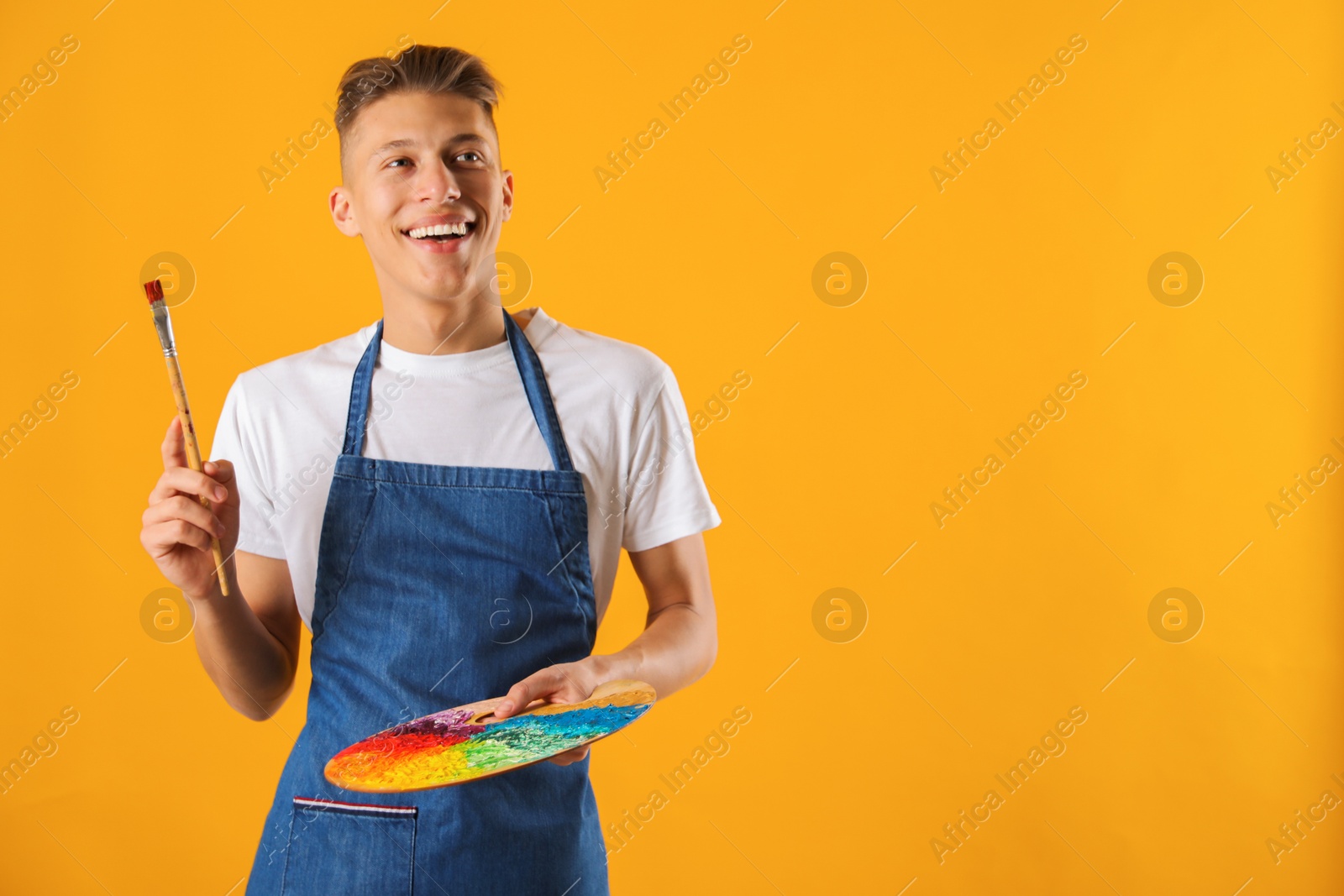 Photo of Happy man with palette and paintbrush on orange background. Space for text