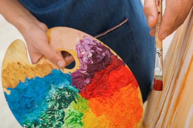 Photo of Man with palette and paintbrush drawing picture, closeup