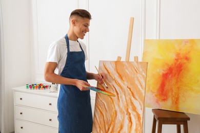 Photo of Smiling man with palette and paintbrush drawing picture indoors