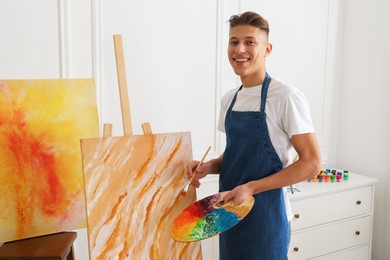 Photo of Smiling man with palette and paintbrush drawing picture indoors