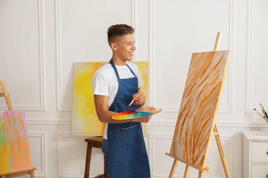 Photo of Smiling man with palette and paintbrush drawing picture indoors