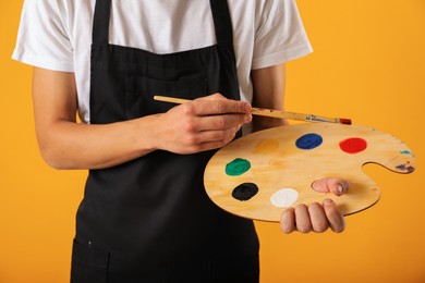 Photo of Man with wooden palette and paintbrush on orange background, closeup