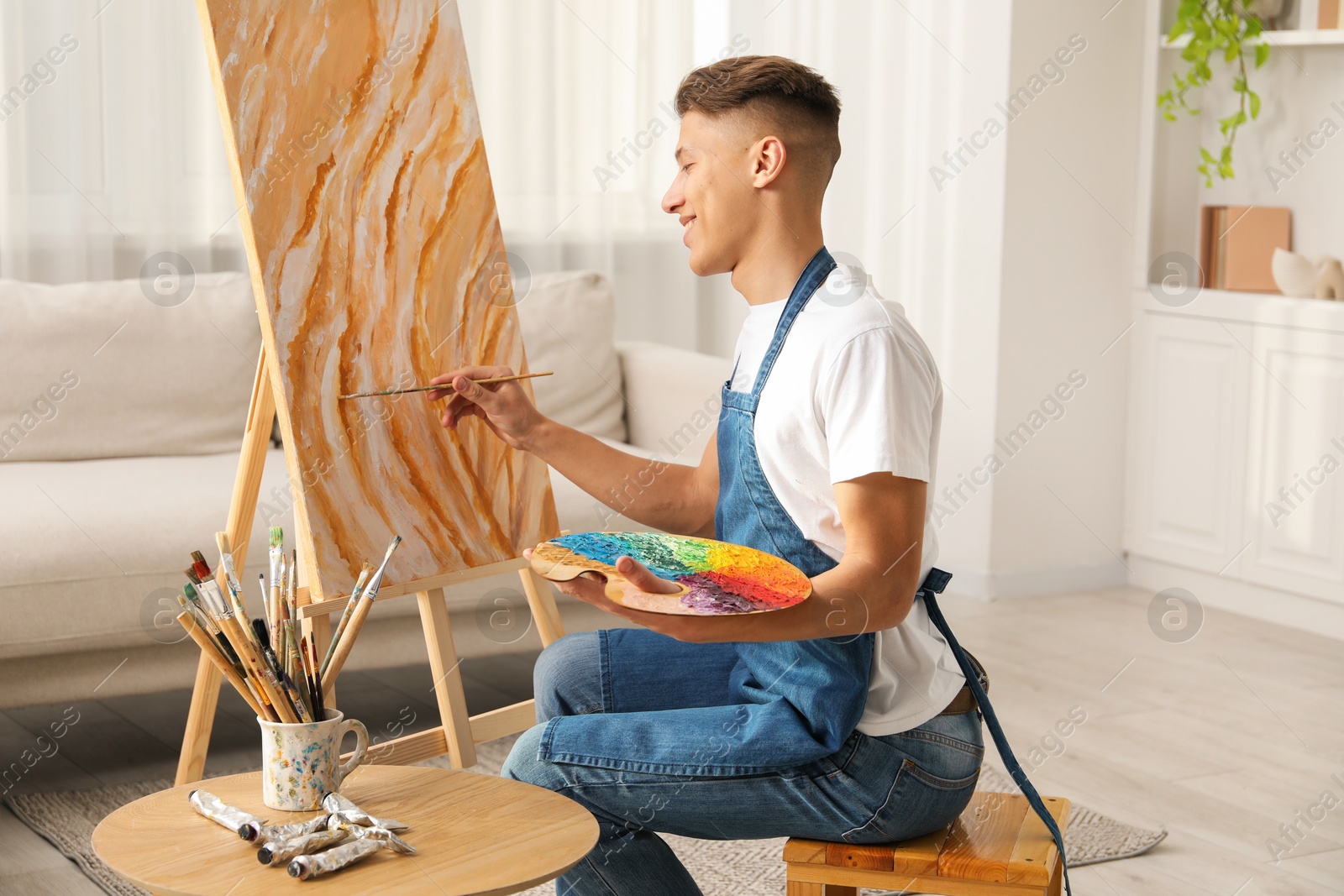 Photo of Smiling man with palette and paintbrush drawing picture indoors