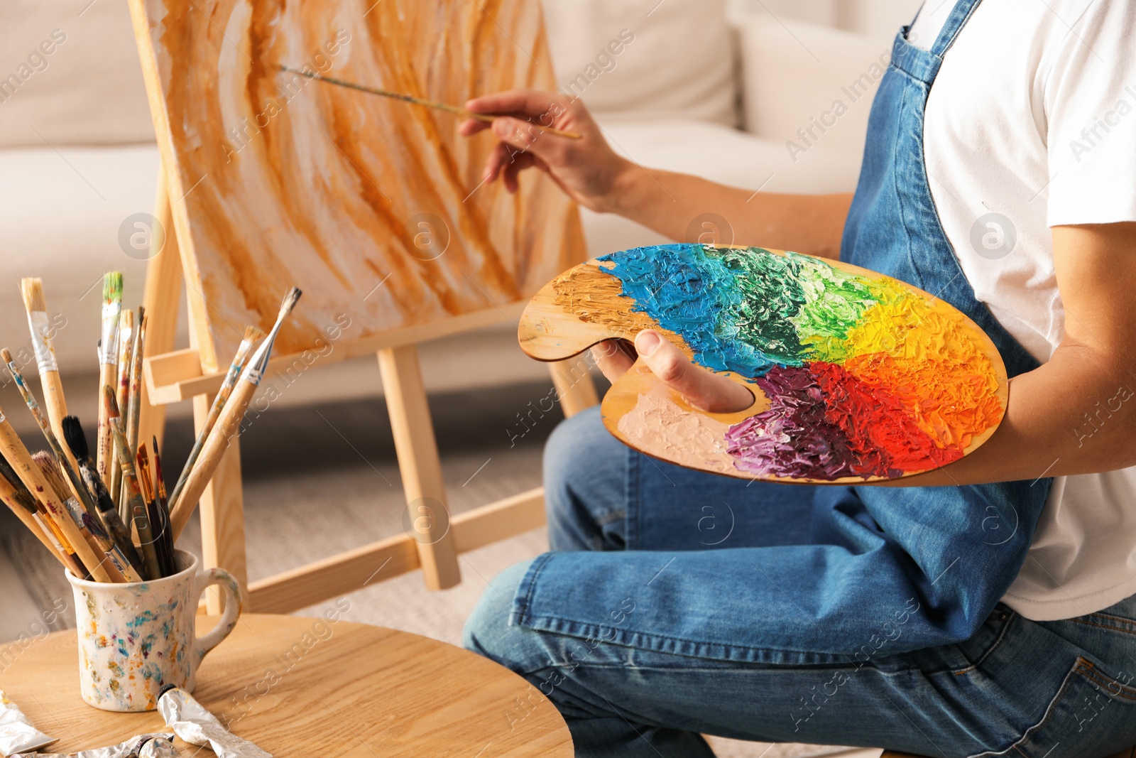 Photo of Man with palette and paintbrush drawing picture indoors, closeup