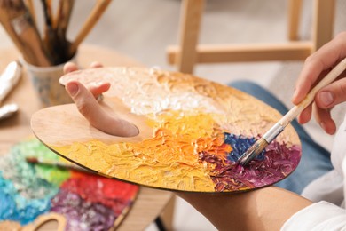 Photo of Man with paintbrush mixing paints on palette indoors, closeup