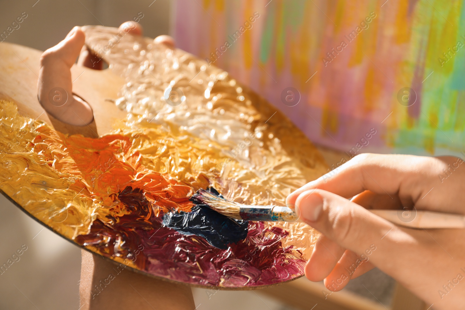 Photo of Man with paintbrush mixing paints on palette indoors, closeup