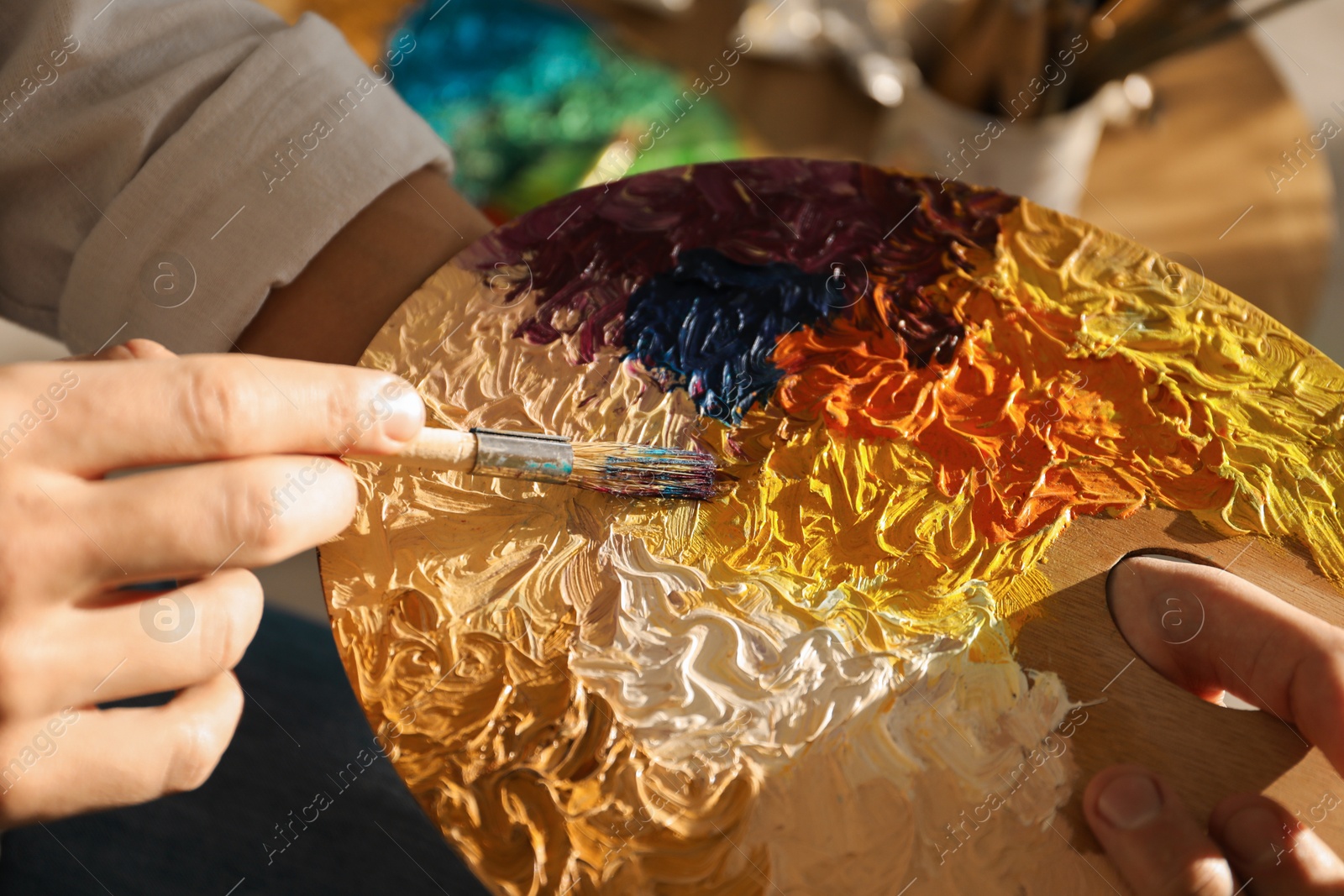 Photo of Man with paintbrush mixing paints on palette indoors, closeup