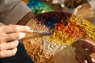 Photo of Man with paintbrush mixing paints on palette indoors, closeup