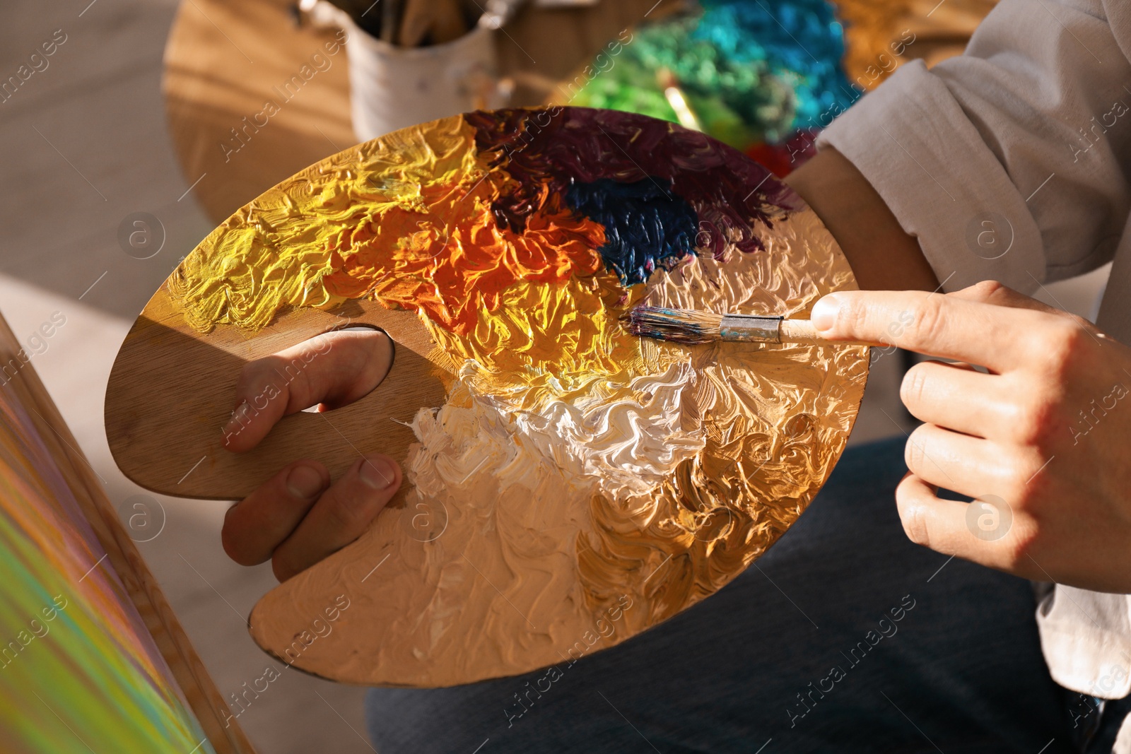 Photo of Man with paintbrush mixing paints on palette indoors, closeup