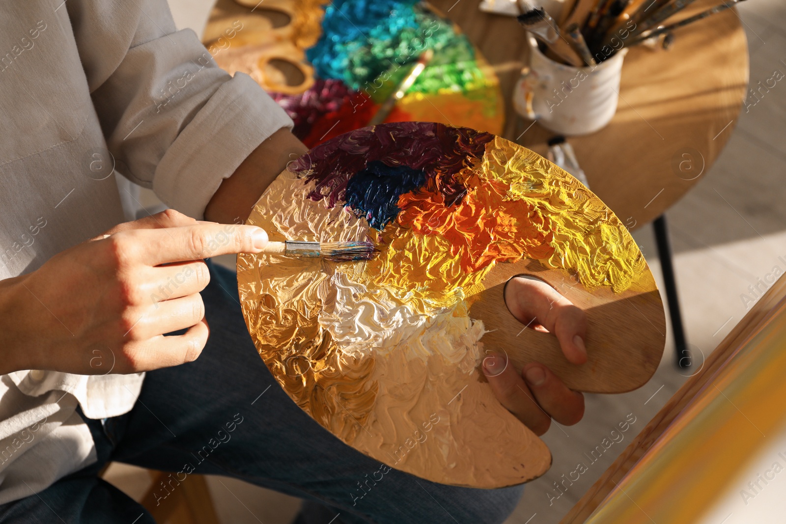 Photo of Man with paintbrush mixing paints on palette indoors, closeup