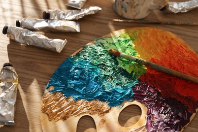 Photo of Palette with bright paints, brush and tubes on wooden table, above view