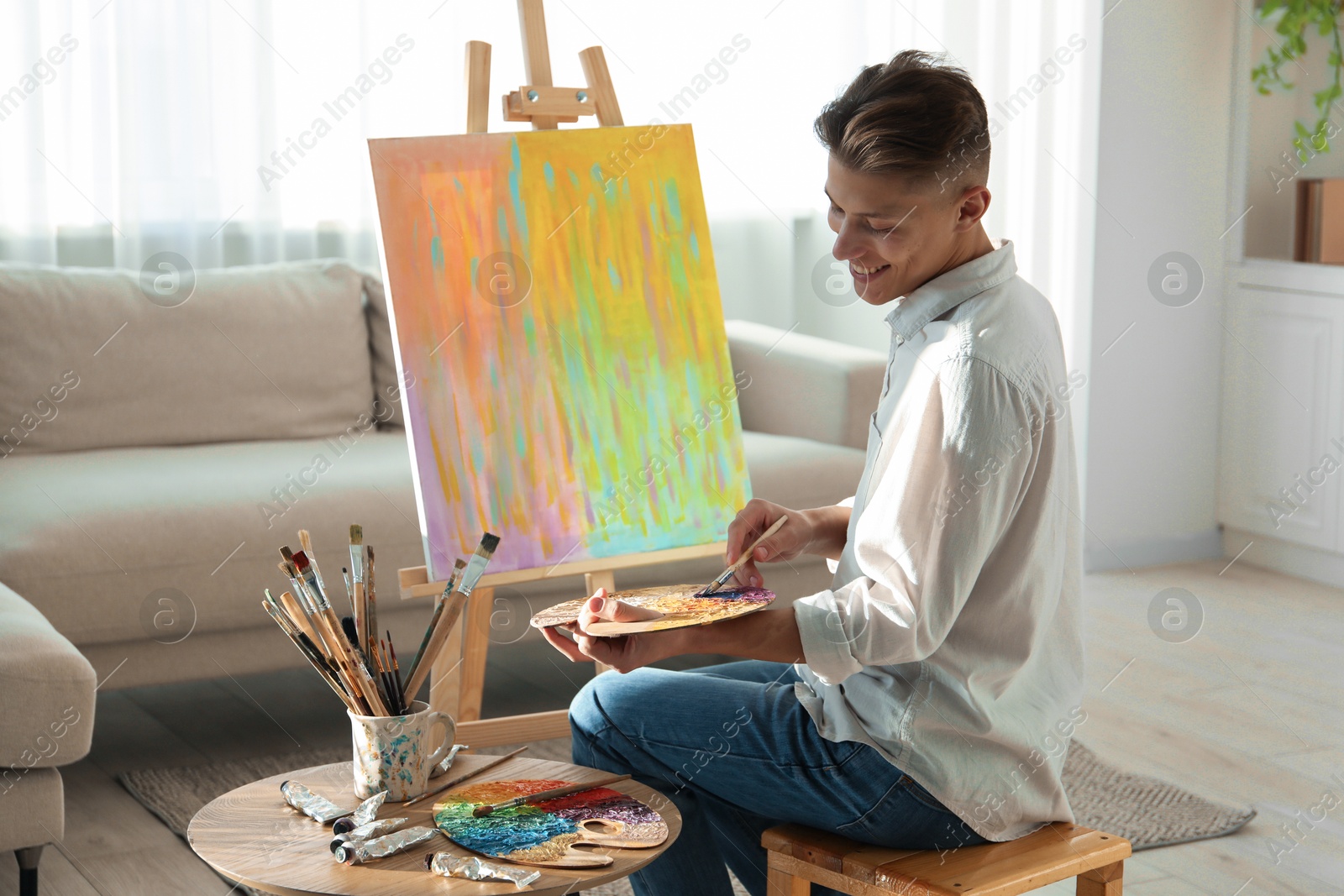 Photo of Smiling man with palette and paintbrush drawing abstract picture at home