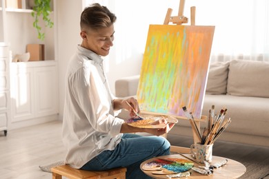 Photo of Smiling man with palette and paintbrush drawing abstract picture at home