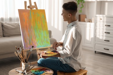 Photo of Man with palette and paintbrush drawing abstract picture at home