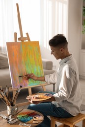 Photo of Man with palette and paintbrush drawing abstract picture at home