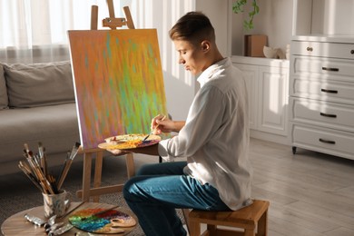 Photo of Man with palette and paintbrush drawing abstract picture at home