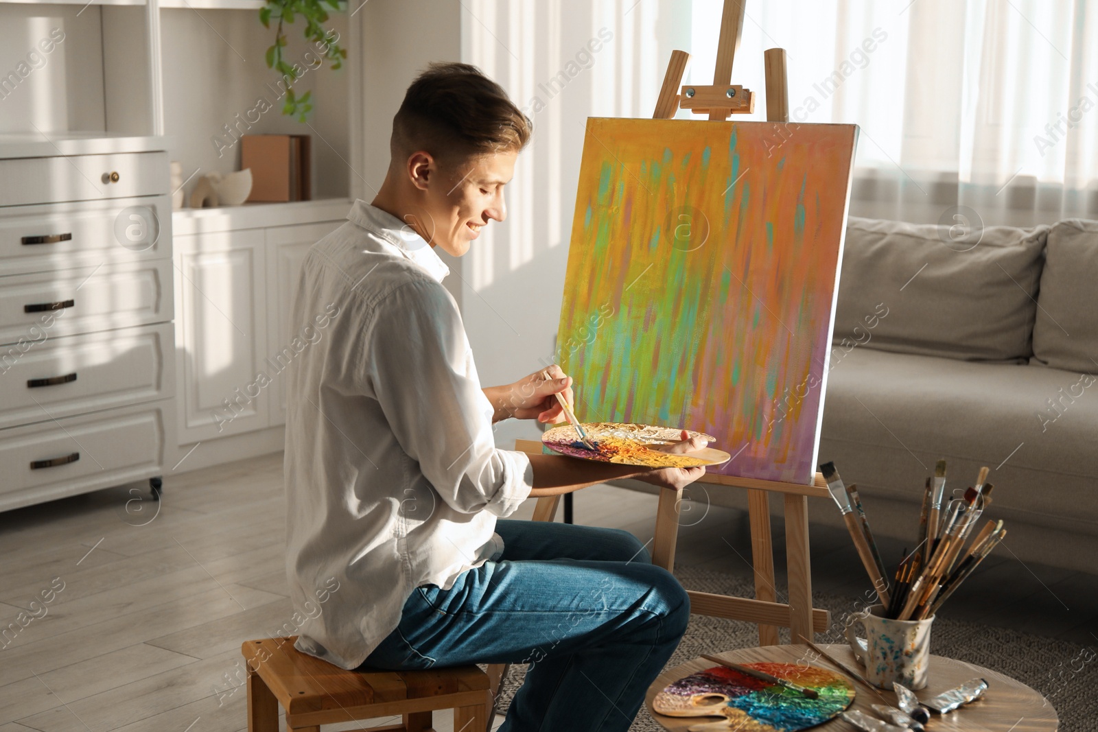 Photo of Smiling man with palette and paintbrush drawing abstract picture at home