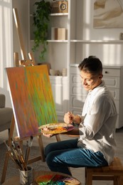 Photo of Smiling man with palette and paintbrush drawing abstract picture at home