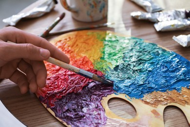 Photo of Man with paintbrush mixing paints on palette at wooden table, closeup