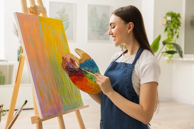 Photo of Smiling woman with palette and paintbrush drawing abstract picture