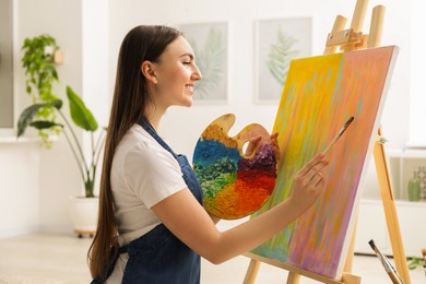 Smiling woman with palette and paintbrush drawing abstract picture