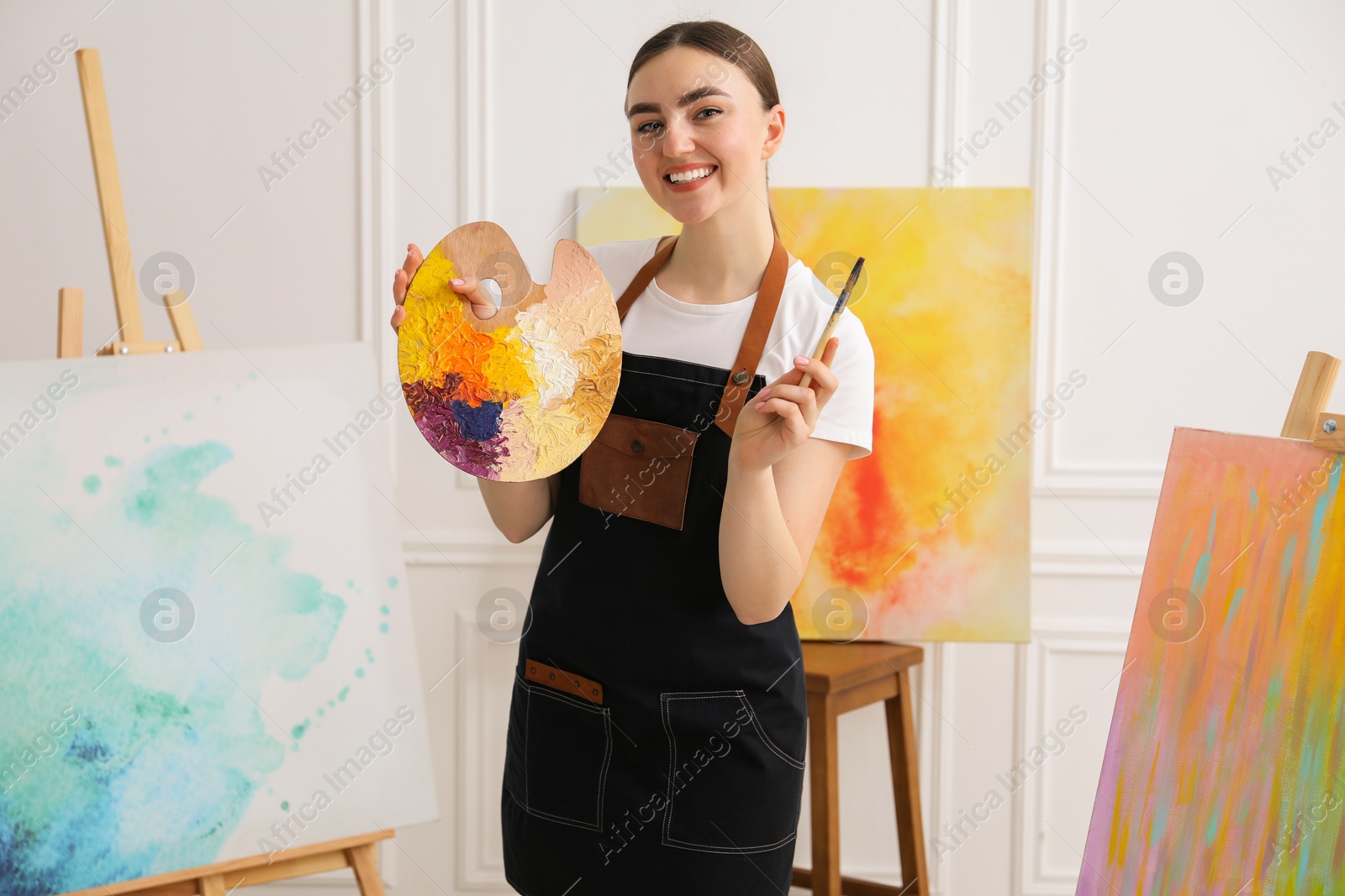 Photo of Smiling woman with palette and paintbrush in workshop