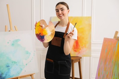 Photo of Smiling woman with palette and paintbrush in workshop