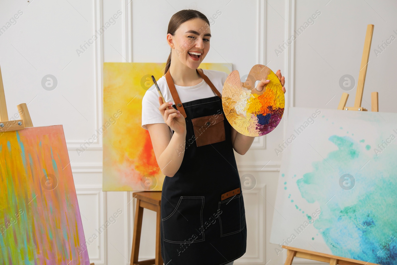 Photo of Happy woman with palette and paintbrush in workshop