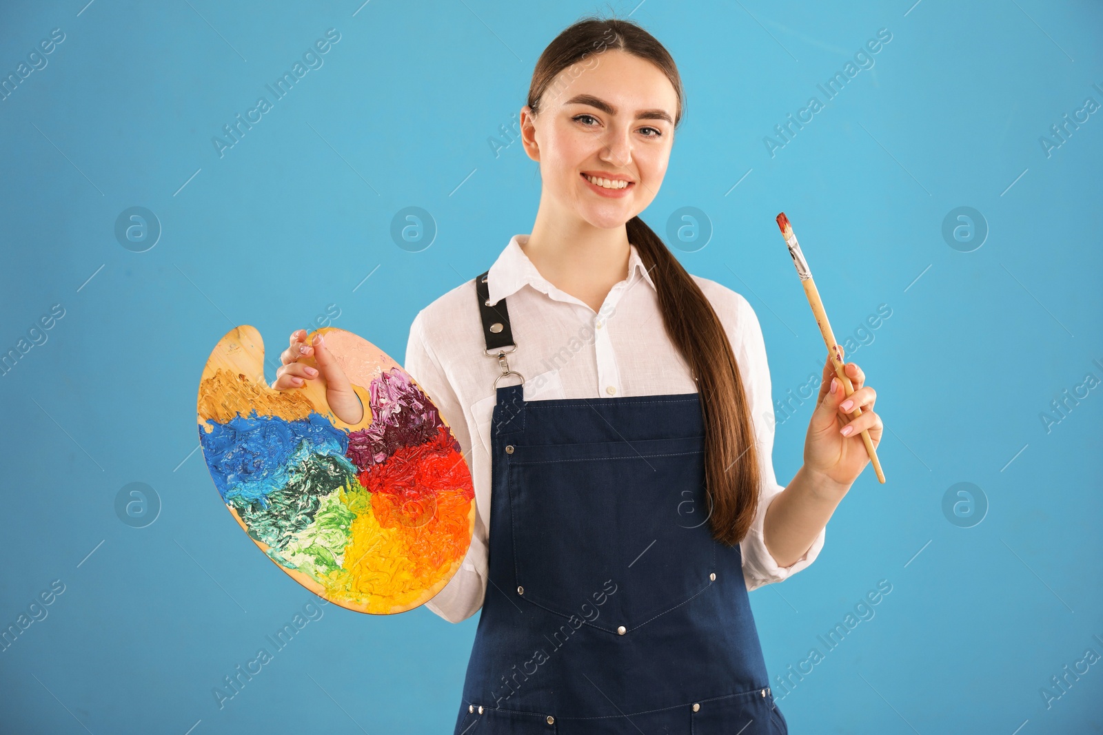 Photo of Smiling woman with palette and paintbrush on light blue background