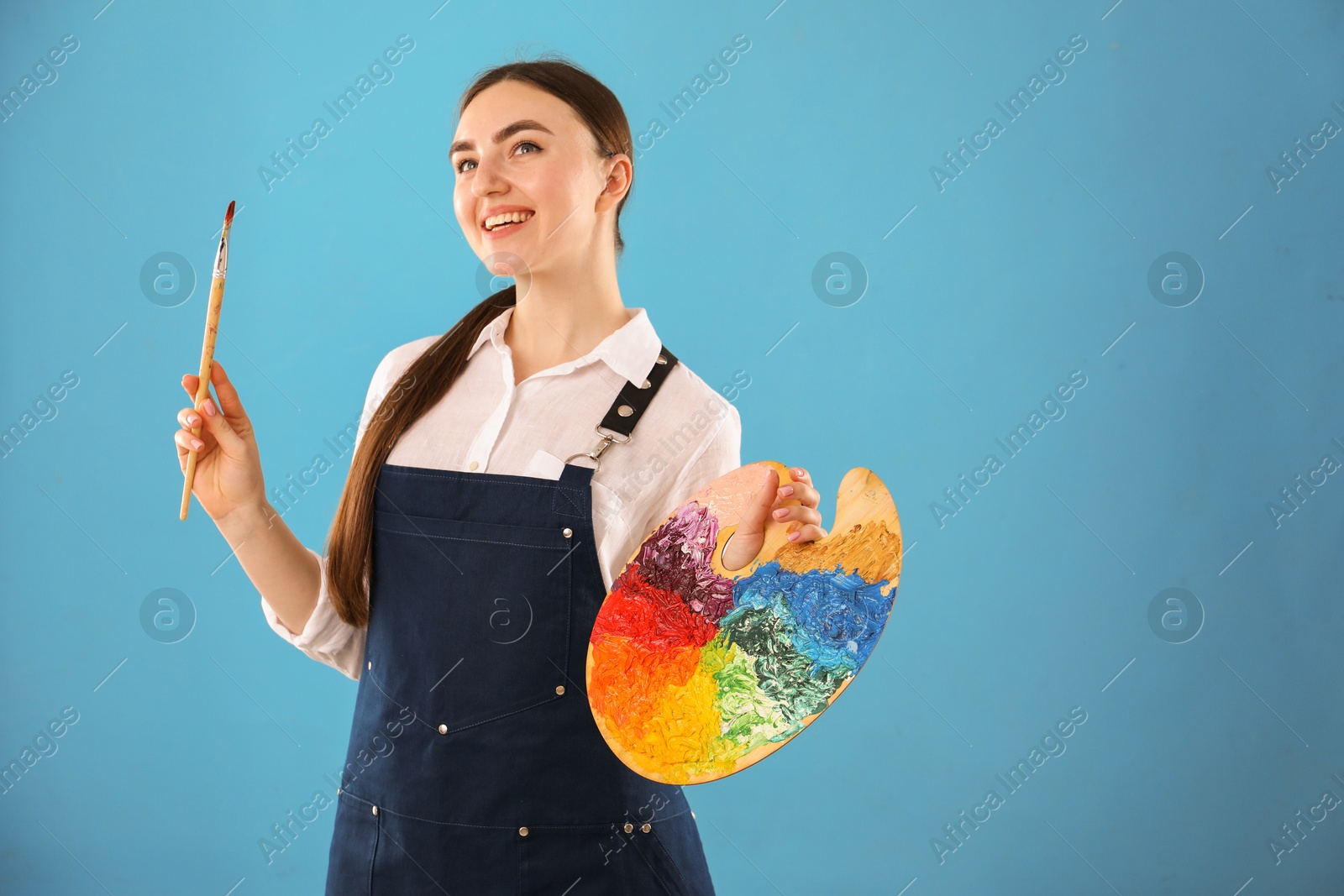 Photo of Smiling woman with palette and paintbrush on light blue background. Space for text