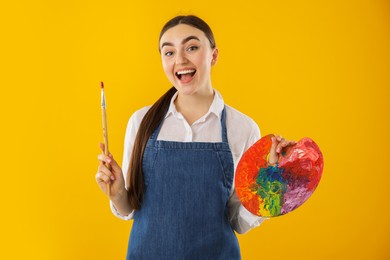 Photo of Happy woman with palette and paintbrush on orange background