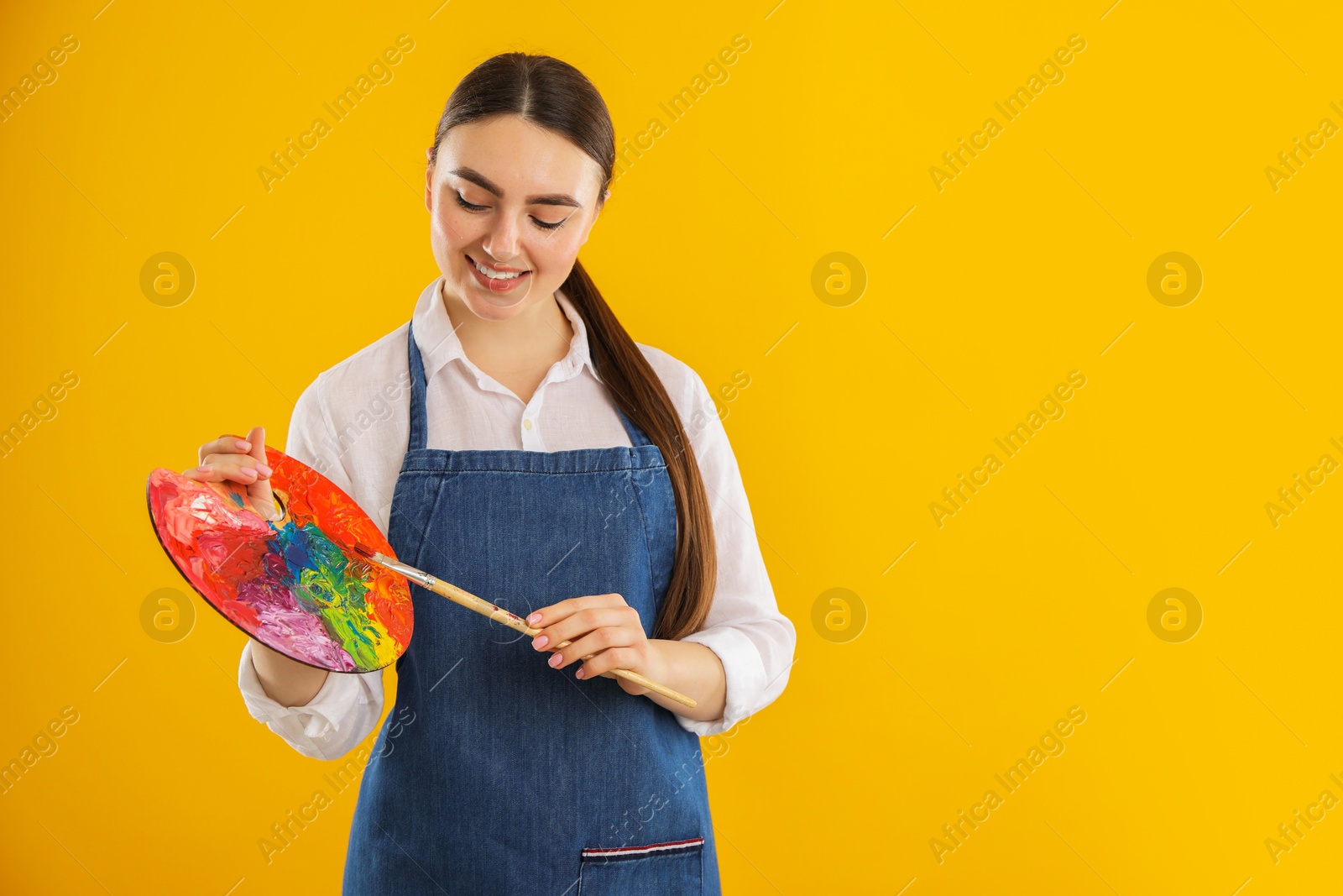 Photo of Smiling woman with palette and paintbrush on orange background. Space for text