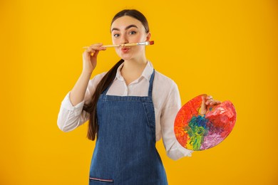 Woman with palette and paintbrush on orange background