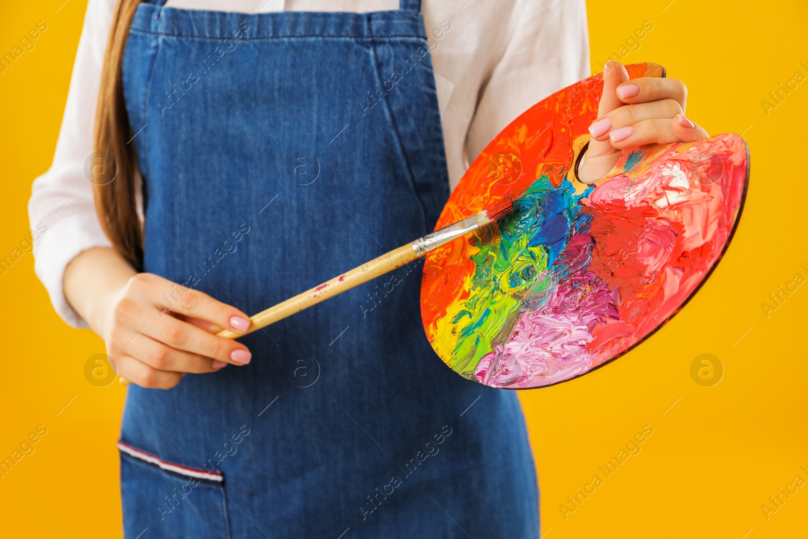 Photo of Woman with palette and paintbrush on orange background, closeup