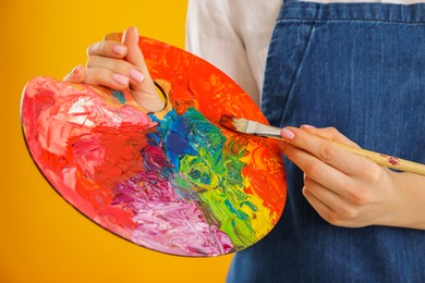 Photo of Woman with palette and paintbrush on orange background, closeup