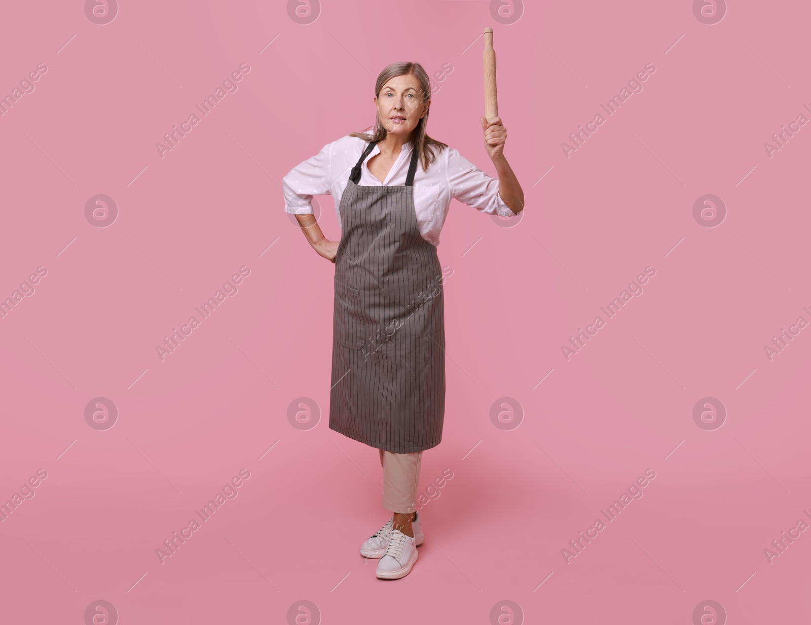 Photo of Emotional woman with rolling pin on pink background