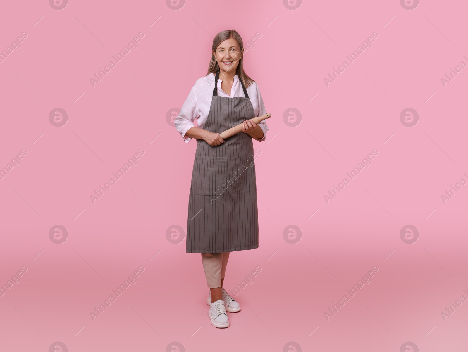 Photo of Happy woman with rolling pin on pink background