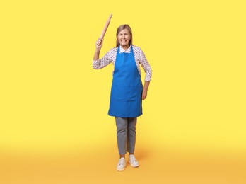 Photo of Angry woman with rolling pin on yellow background