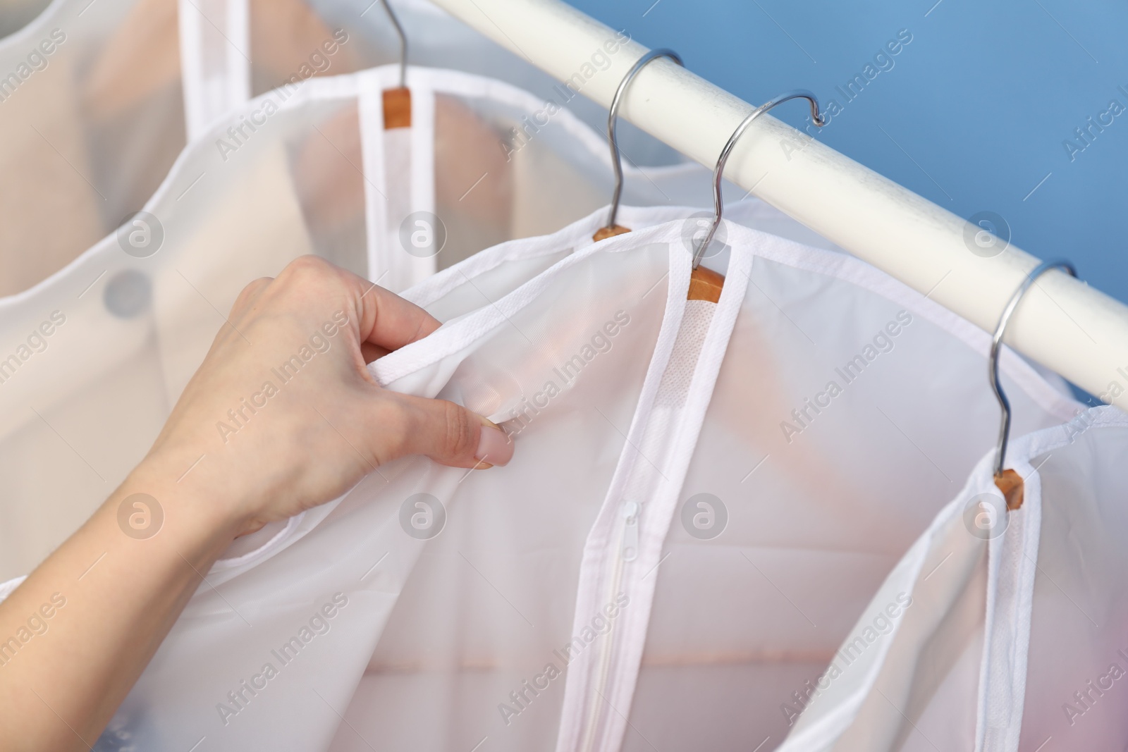 Photo of Woman taking garment cover with clothes from rack indoors, closeup