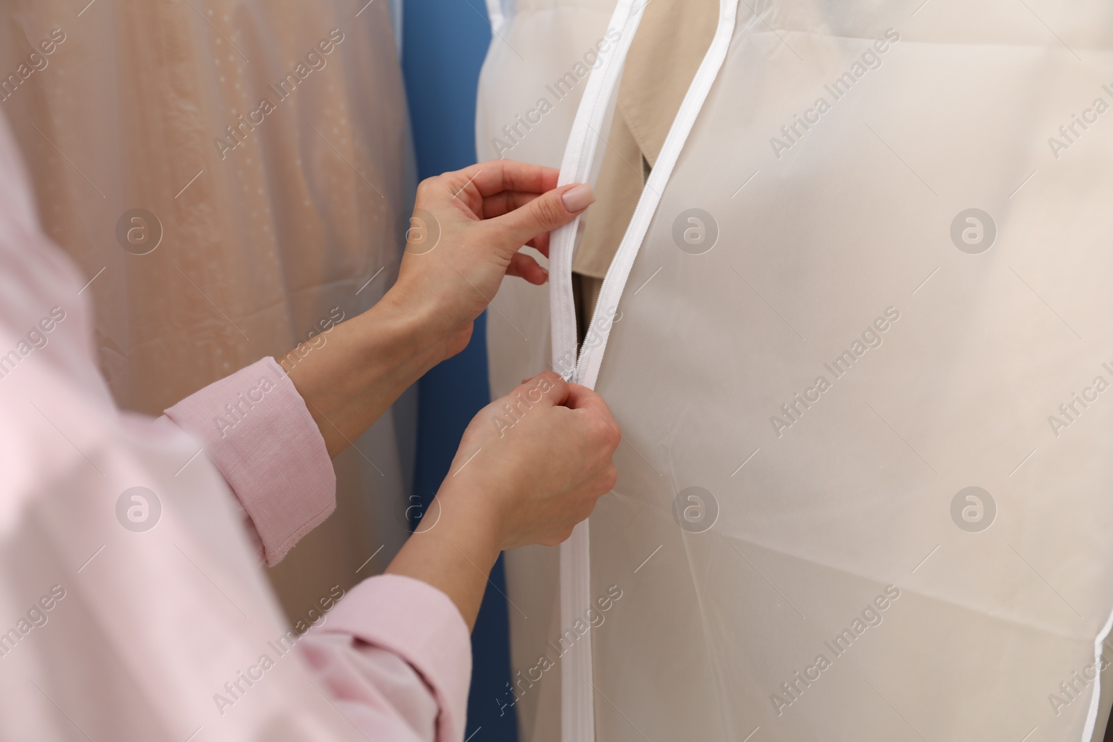 Photo of Woman zipping garment cover with clothes indoors, closeup